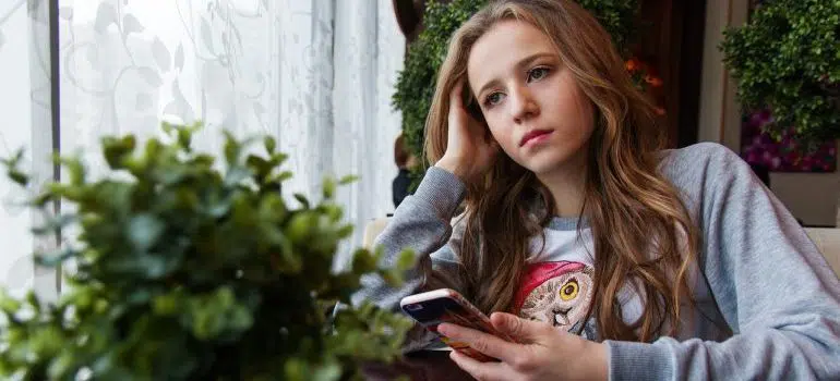 A woman thinking about something while holding a phone.